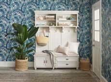 White entryway unit with cushion and throw plus houseplant surround and blue wallpaper