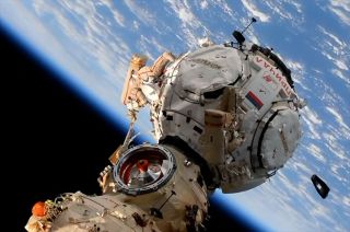 prichal module of international space station with cosmonauts doing a spacewalk. a container floats away at lower right