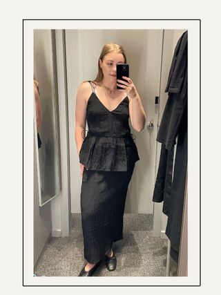 Woman in dressing room wears crinkle black top, crinkle black skirt and black ballet flats