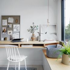 Neutral l home office with wooden desk and decorated with pin board decor, plants, and lighting