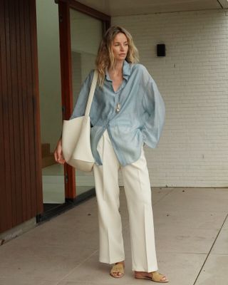 @anoukyve wearing a blue button down skirt, cream trousers, a cream leather tote bag, and silver pendant necklace