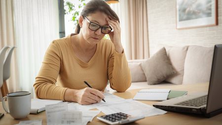 A woman looks focused as she works on her taxes at her dining room table.
