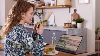 Woman eating a sandwich in a kitchen while watching a movie on a laptop