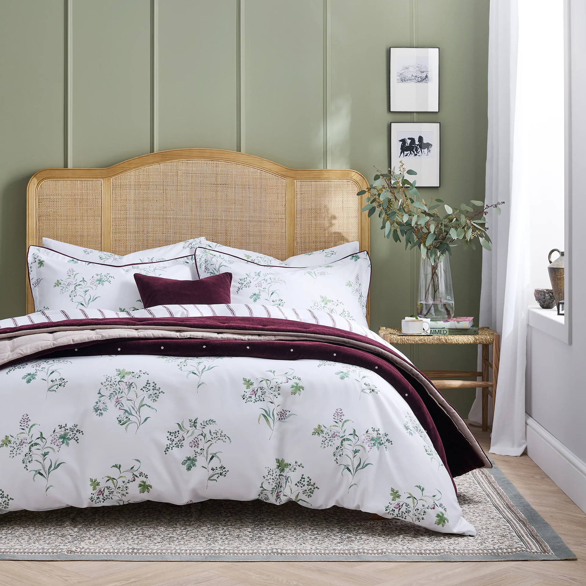 Image of a rattan bed with white floral bedding a a burgundy throw.