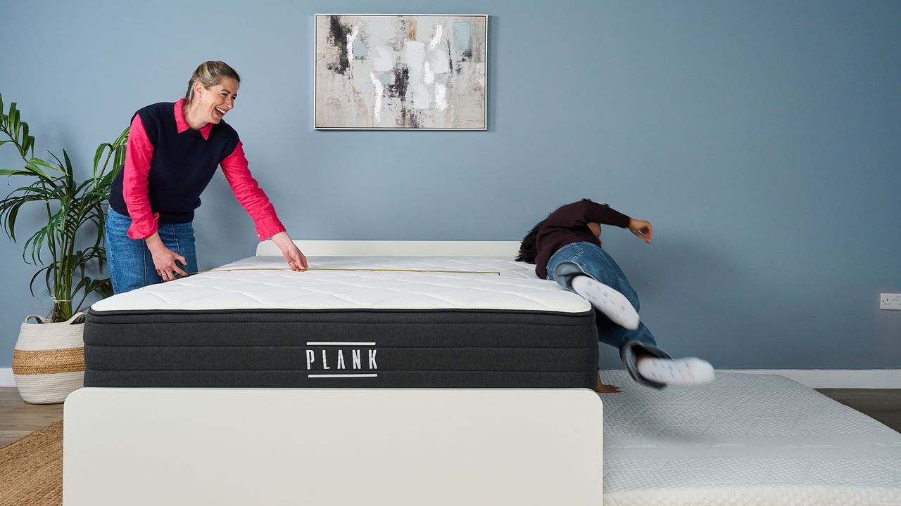Testing the edge support of the Plank Firm Luxe mattress in our Sleep Lab. On the left, Nicola Appleton uses a tape measure to see how close Becky George is to the edge of the bed. On the right, Becky George is falling off the mattress on to a waiting crash pad