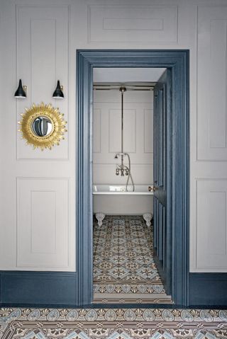 Light grey bathroom with freestanding bath, patterned tile floor and blue skirting and door