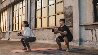 Two people holding a dumbbell squat