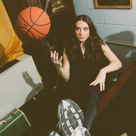 The Seattle Storm's Nika Mühl sitting in a desk chair wearing Under Armour sneakers while playing with a basketball.