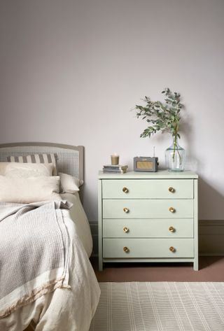 Bedroom with soft pink walls, chest of drawers painted soft mint green, and candle