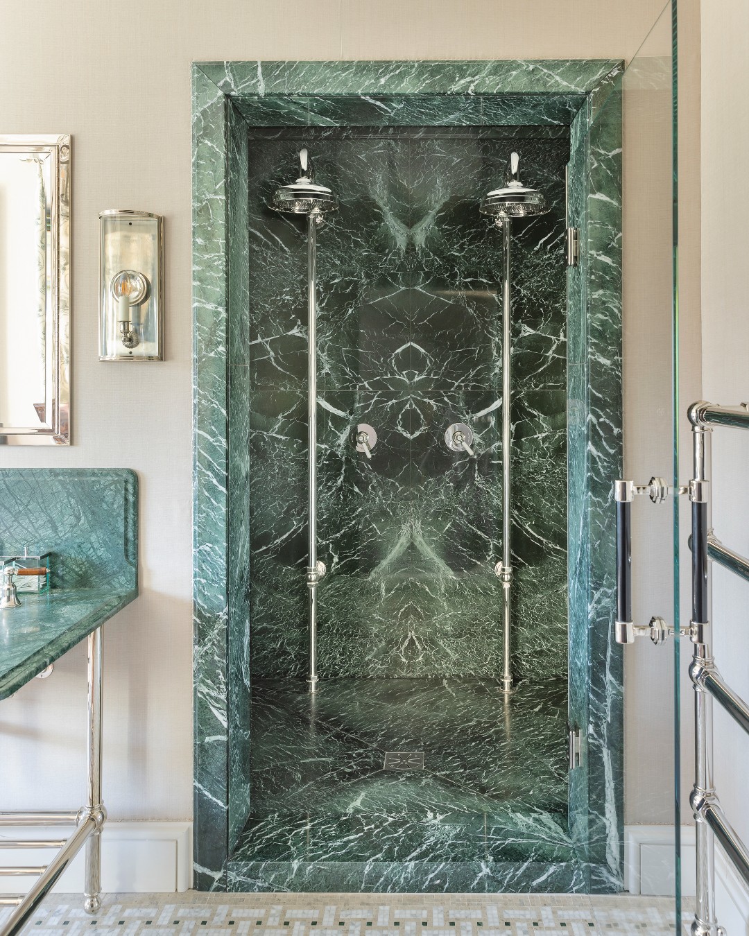 green marble shower enclosure with two shower heads, beige walls, with freestanding vanity and towel rail