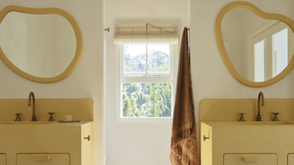 A yellow bathroom with organic shaped mirrors and chequered flooring