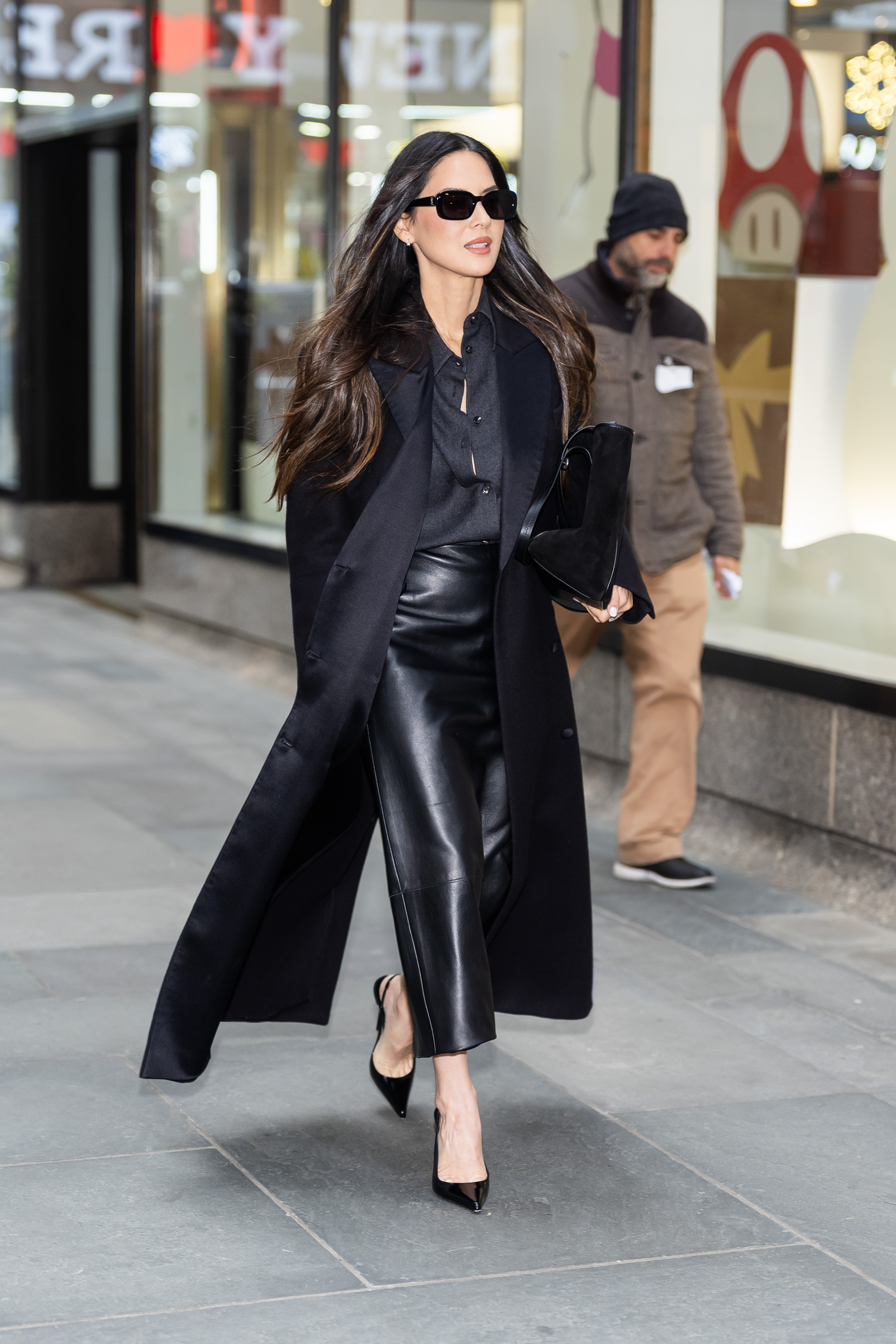 Olivia Munn wearing a black satin coat, black button down, and leather skirt