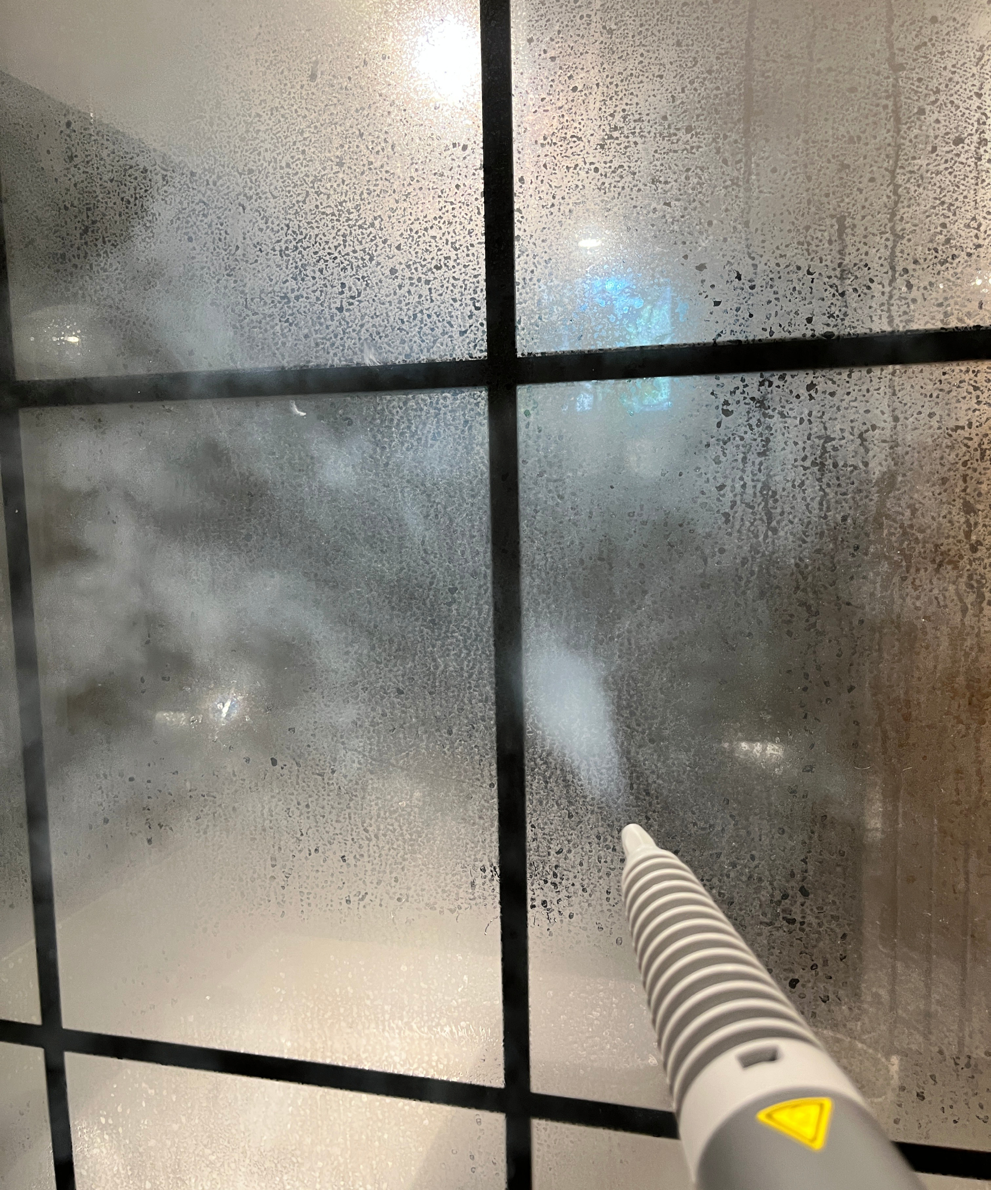 steam cleaner blasting steam at large shower screen with black trim