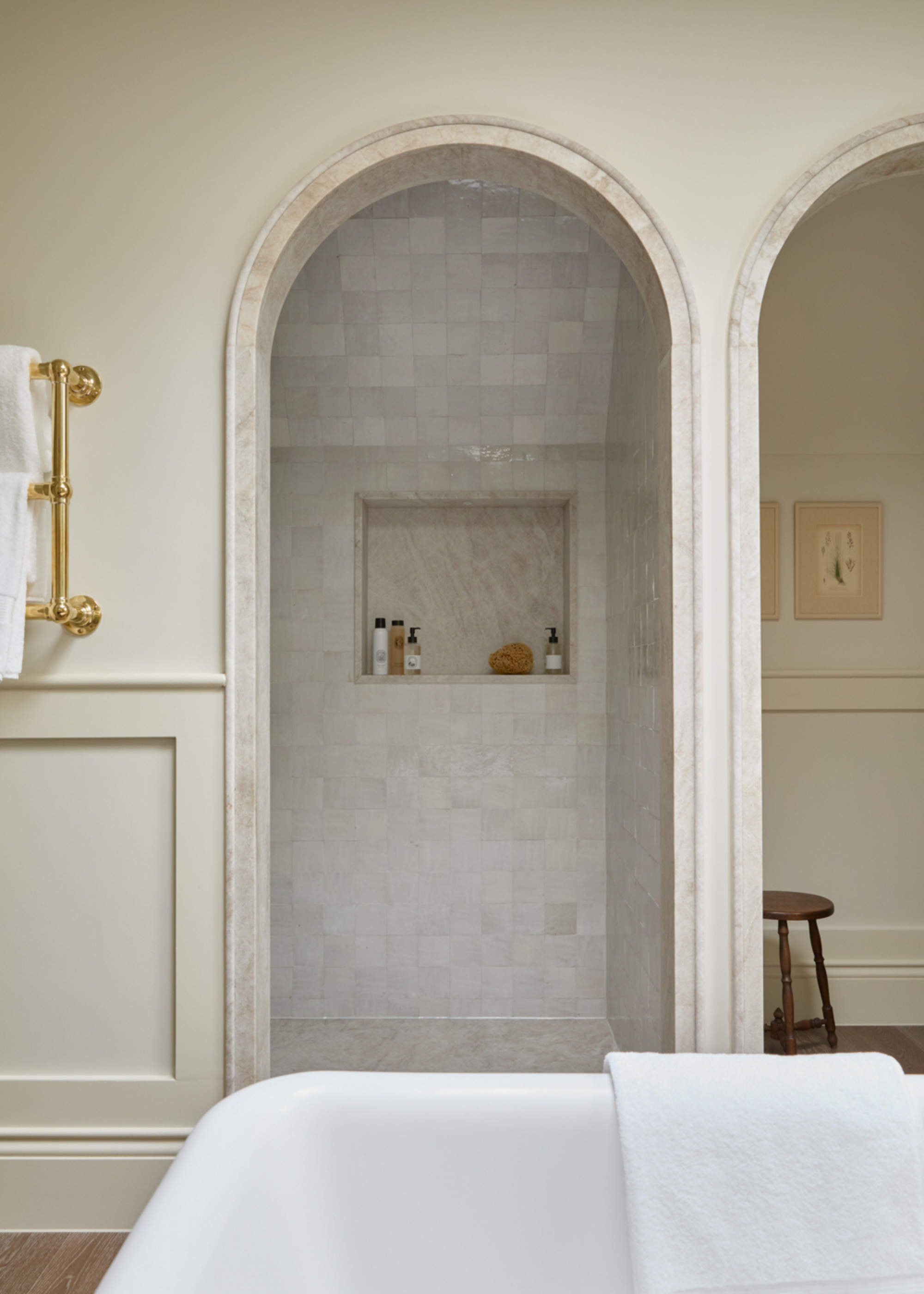 beautiful classical bathroom in neutral tones with an arched marble tiled shower next to an arched doorway