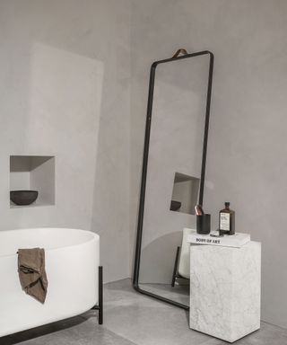 A grey bathroom with concrete effect wall paint decor, floor to ceiling bathroom mirror idea and white bath
