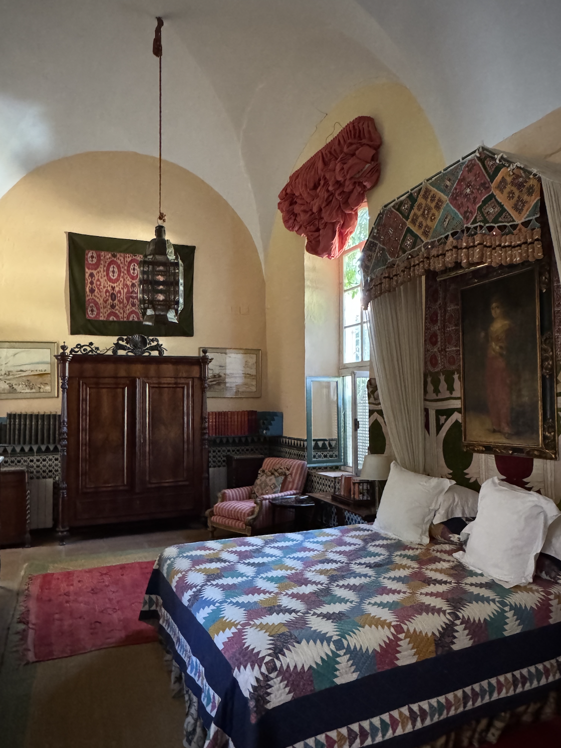 A bed with a colourful throw over it in front of a dark wood cabinet and red rug