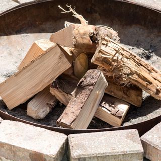 High angle view of firewood in rusty metal bowl of stone fire-pit in garden