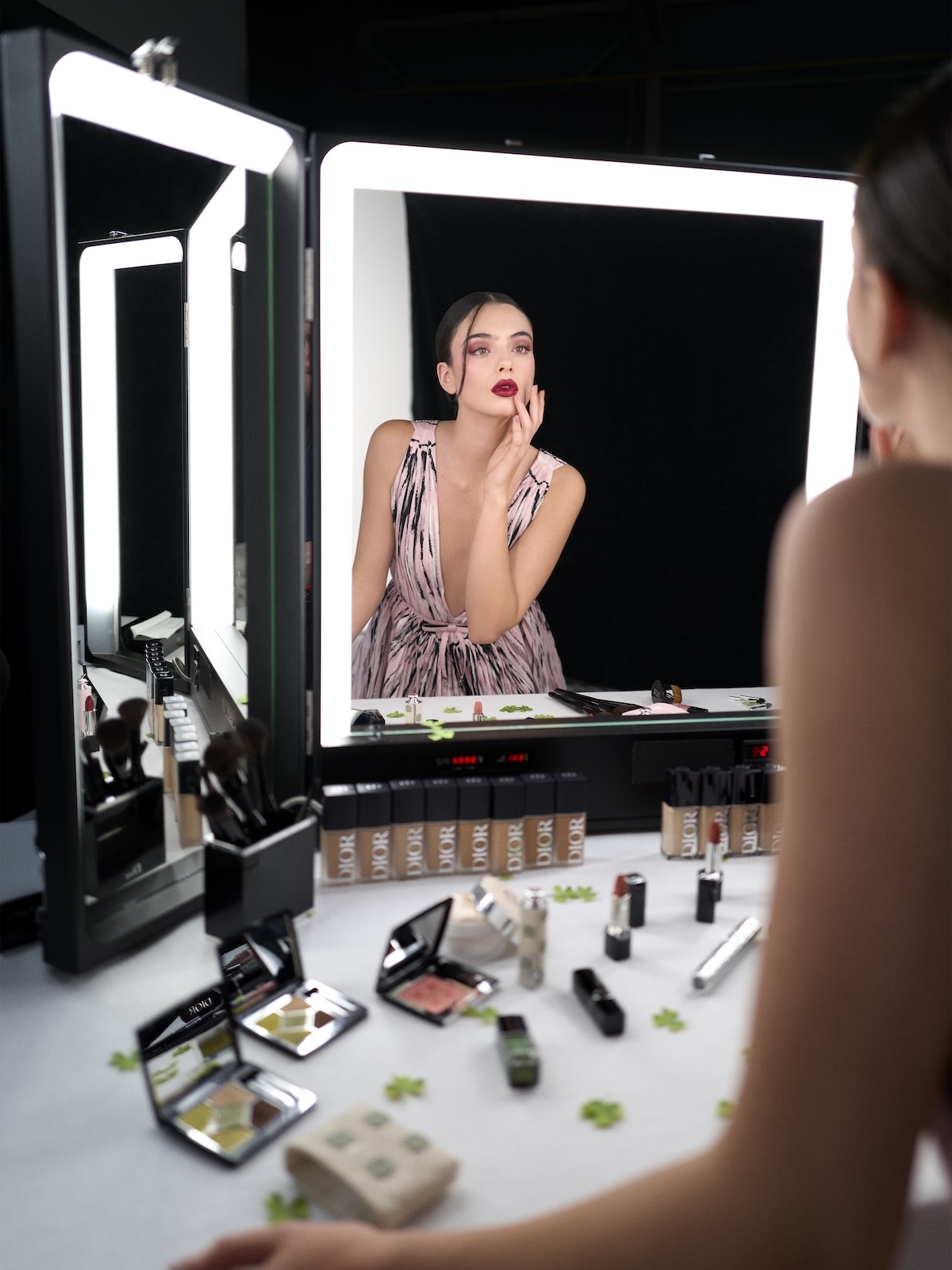 Deva Cassel touching up her makeup in front of a vanity covered in Dior's &amp;quot;Lucky Clover&amp;quot; makeup products.