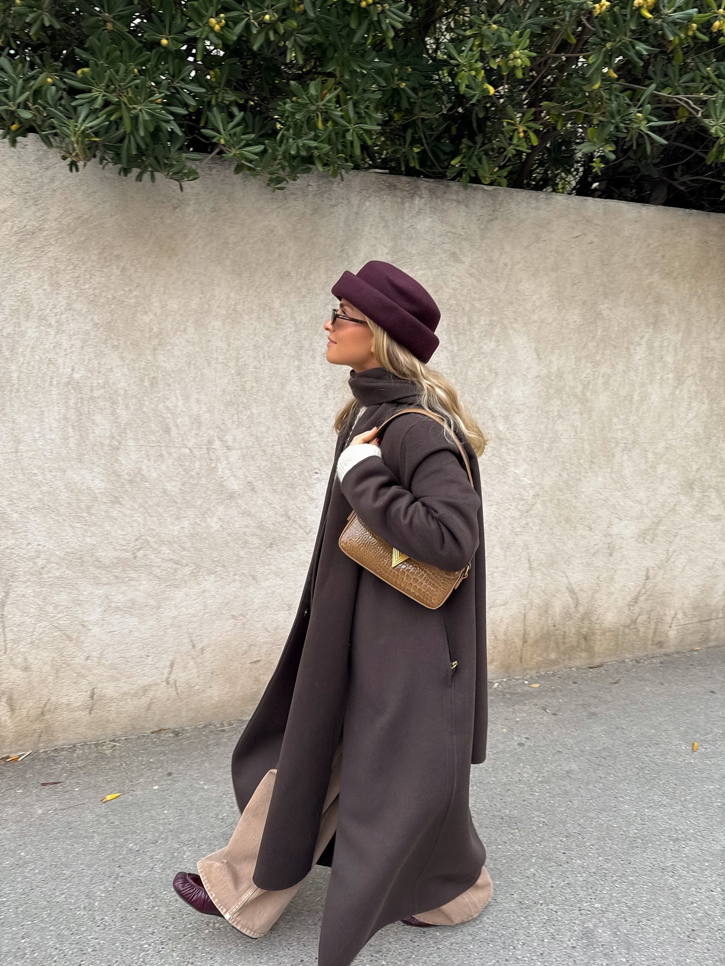 Fashion person Olivia Tps wears a best long wool coat. She wears a brown scarf coat with a dark red hat and loafer. This image was recently taken from her Instagram.