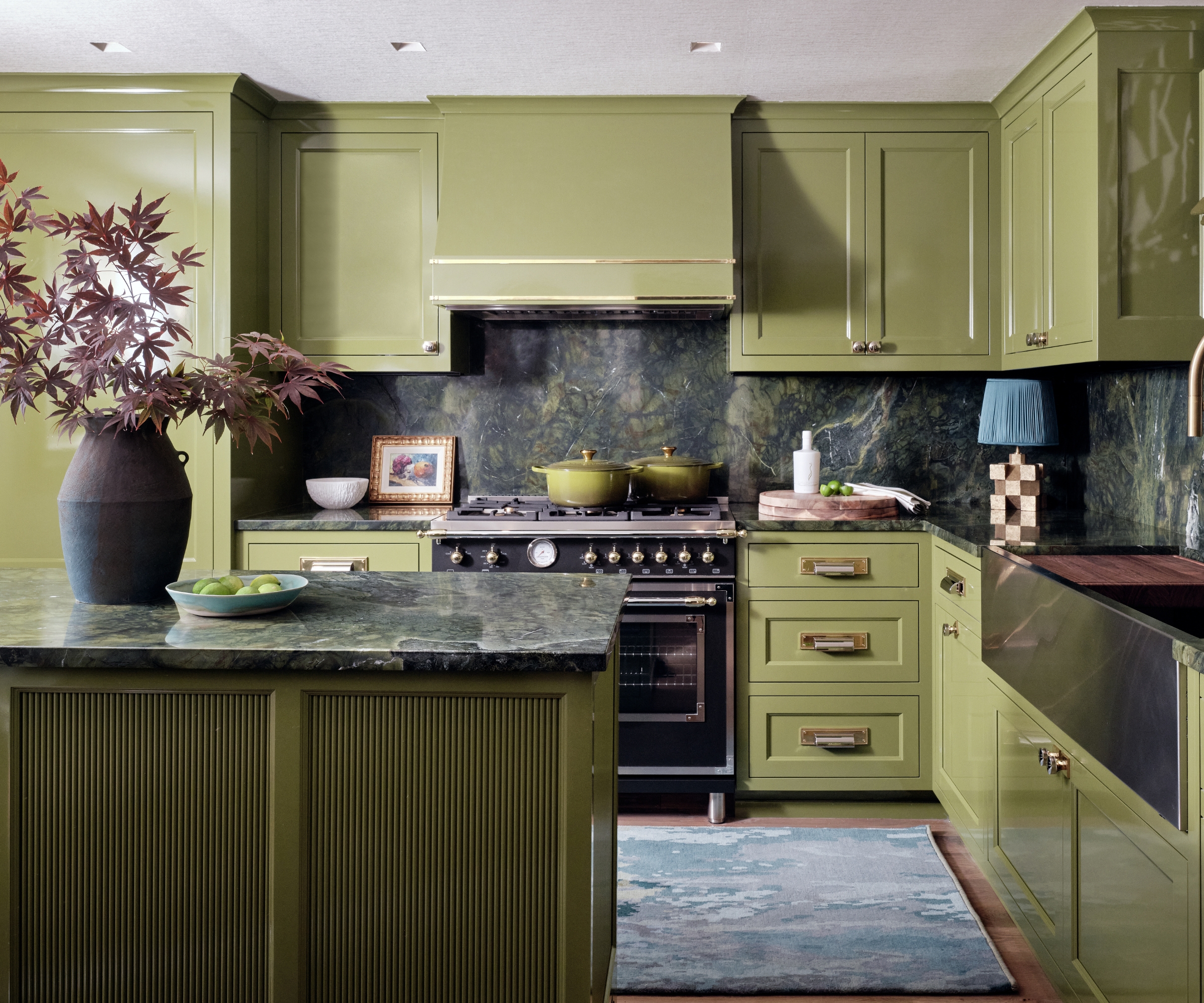 A green kitchen with dark countertops and an antique art piece and countertop lamp