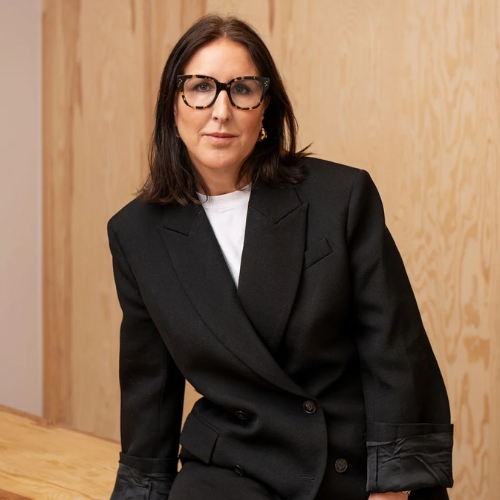 Image of a woman in a black blazer with a white shirt underneath and glasses.