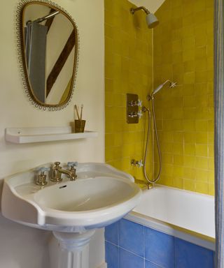 vintage bathroom styled with an ornate pedestal sink, yellow wall tiles, blue bath panel and a vintage rattan mirror