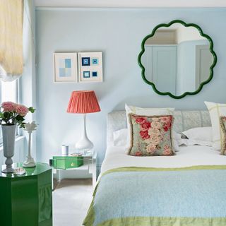 Blue bedroom with oversized bedside lamp, scalloped mirror and floral cushions