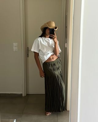 Woman wearing olive green maxi skirt with white t-shirt and cowboy hat.