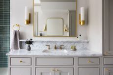 A large grey vanity space with a white marble top in a neutral traditional bathroom with gold accents