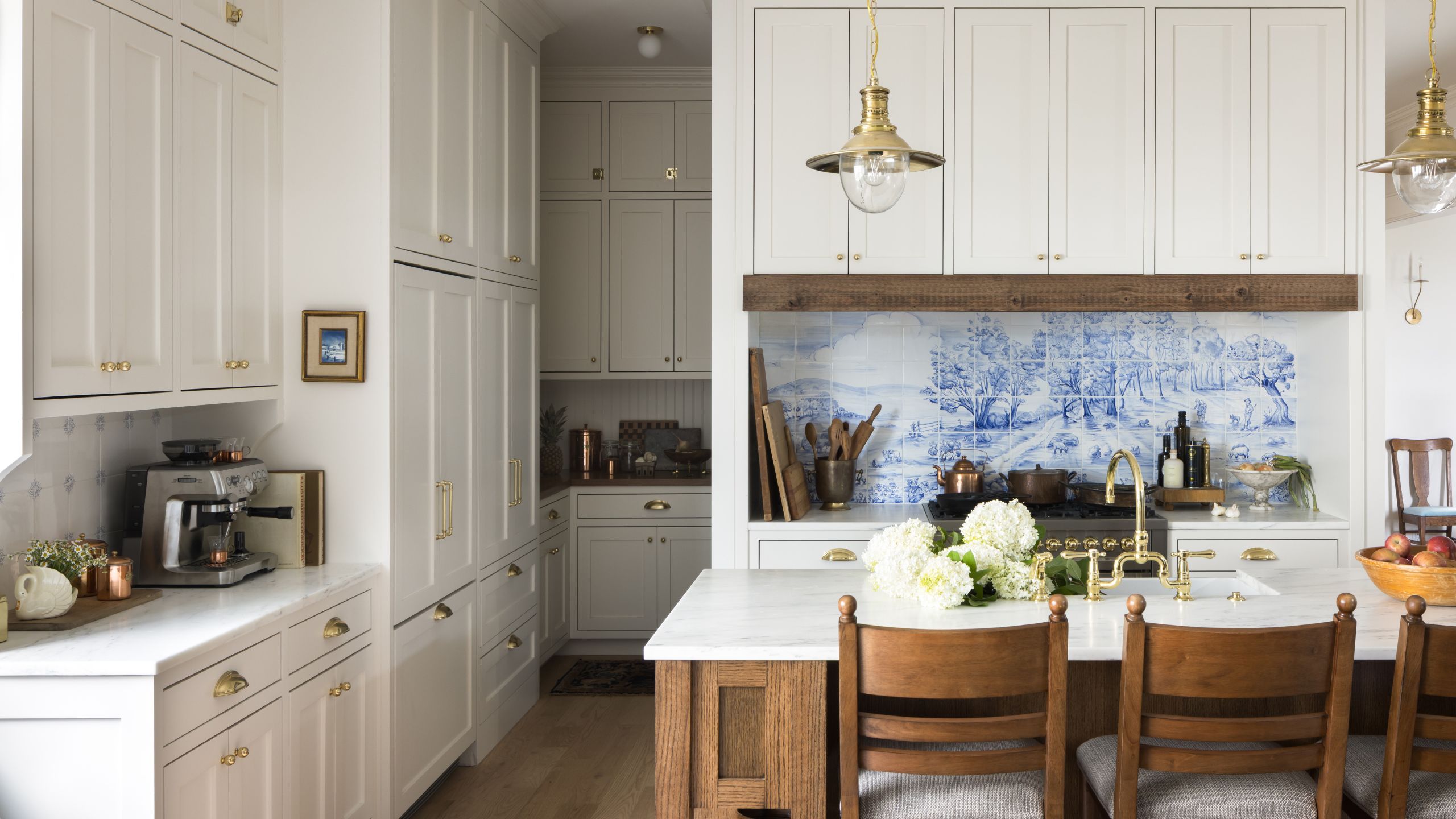 a large white farmhouse kitchen with an oak wooden island, stone countertops, tall cabinetry, and a cooker nook styled with a painted tile mural backsplash