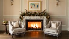 Opulent festive living room featuring ornate picture frame molding, grey accent chairs, lush garland, and a roaring fire