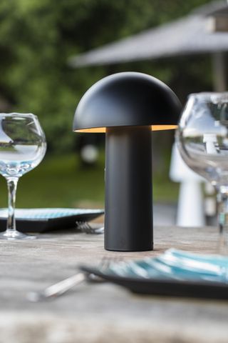 A black tabletop outdoor lamp next to wine glasses