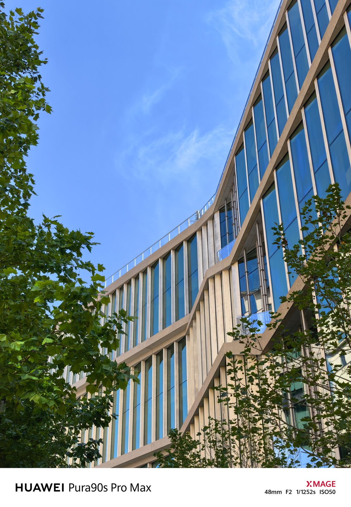 Curved modern building with blue glass windows, framed by green trees beneath a clear blue sky.
