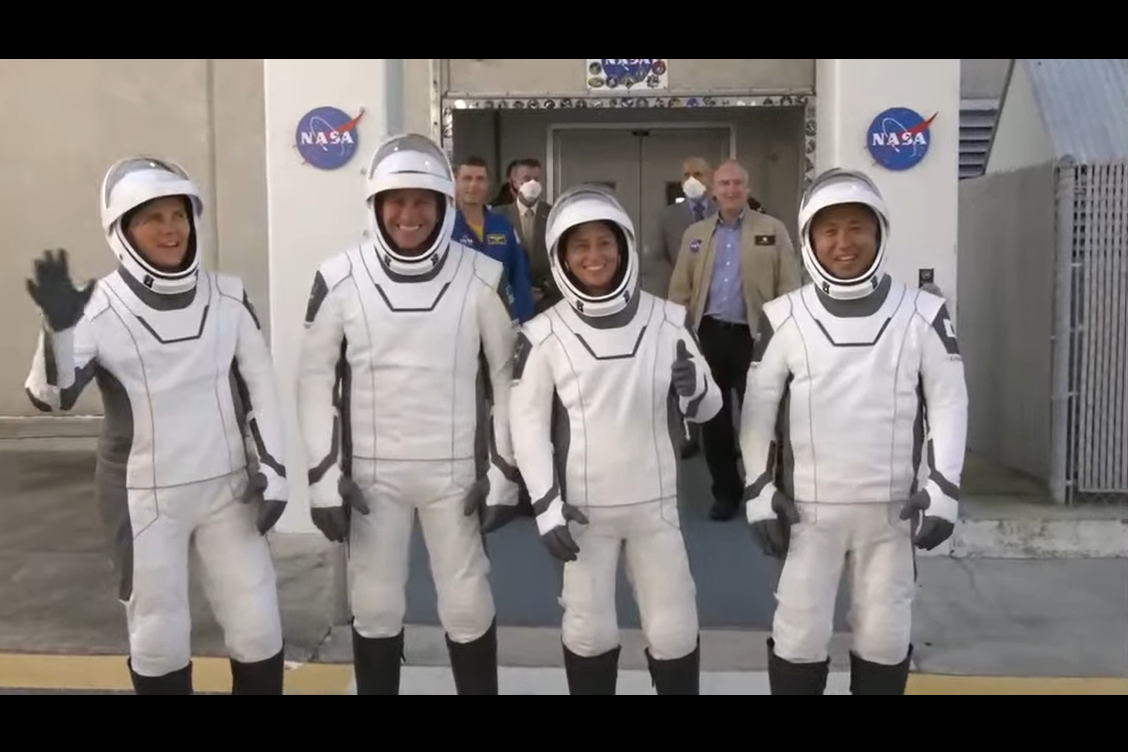 four people in white spacesuits standing in front of a nasa building