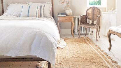 A jute rug with scalloped edges next to a bed with white bedding 