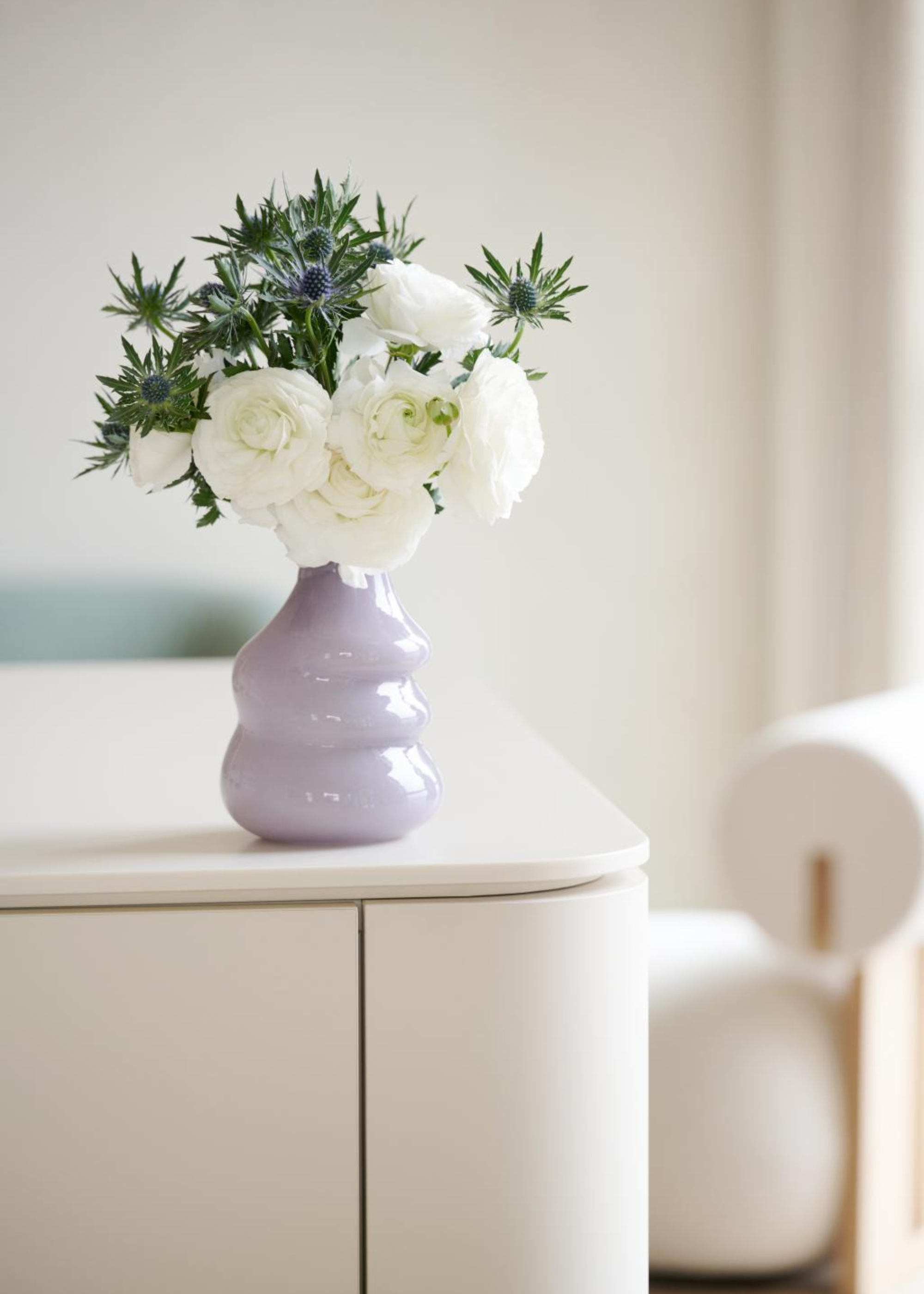 A wavey purple vase with white roses and purple buds on a countertop