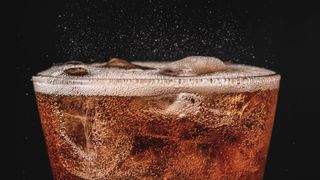 A closeup photo shows cola fizzing in a glass.