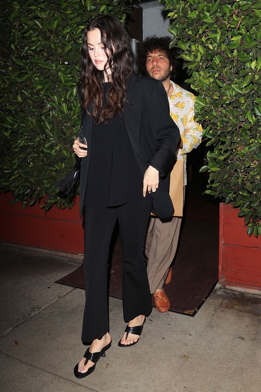 Selena Gomez wearing a black blazer, black cropped pants, and kitten-heel thong sandals with Benny Blanco