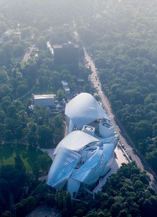 An aerial view of the new Louis Vuitton Foundation in Paris. A large white building made of sail like structures surrounded by trees and with a road next to it.