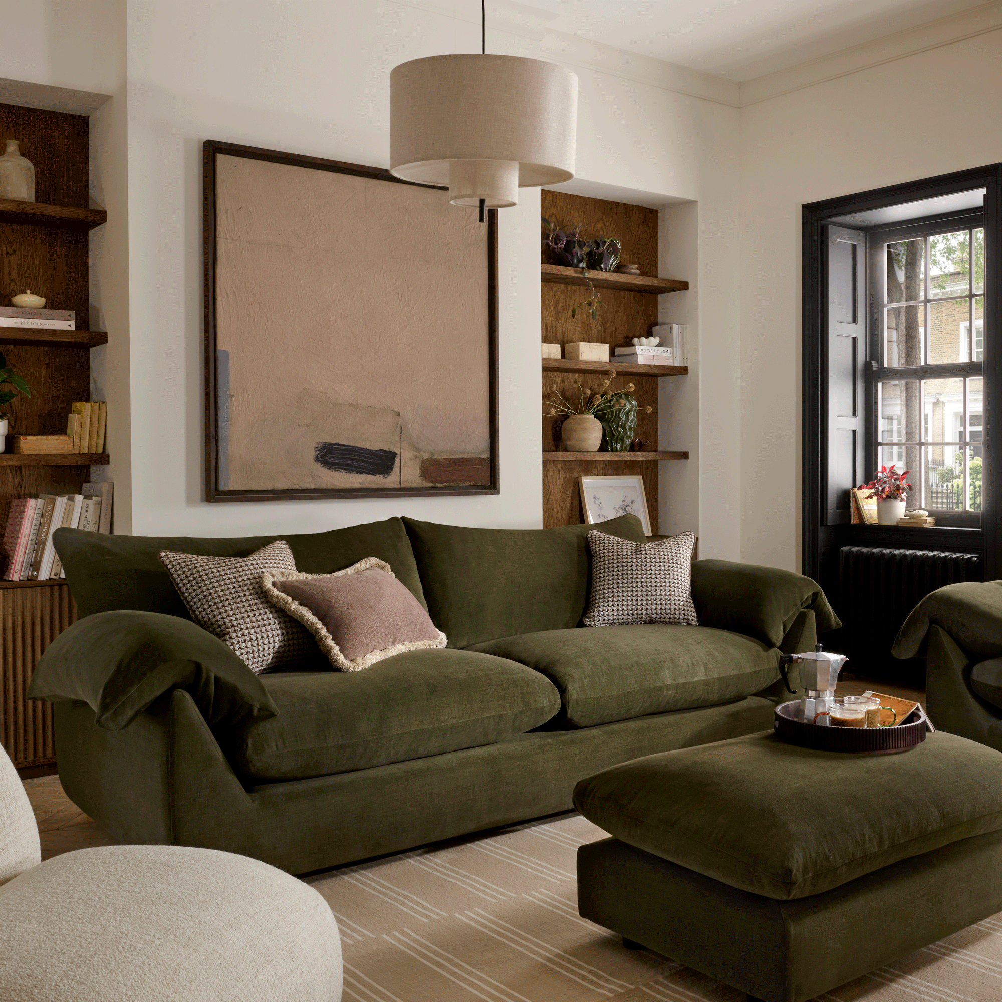 a green velvet sofa and footstool in a neutral living room