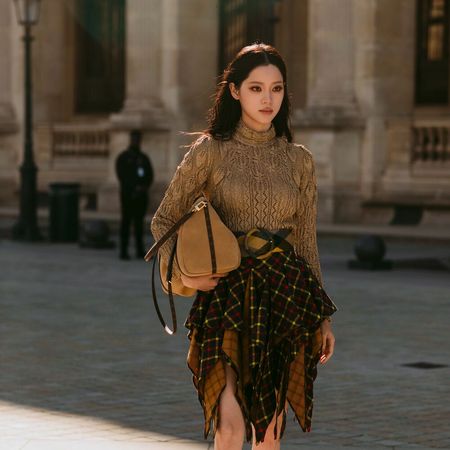 Woman wears brown top and handkerchief hemline skirt, and large suede bag tucked under her arm.