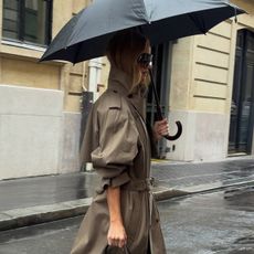 Rosie Huntington Whiteley walking in the rain wearing a trench coat and burgundy boots.