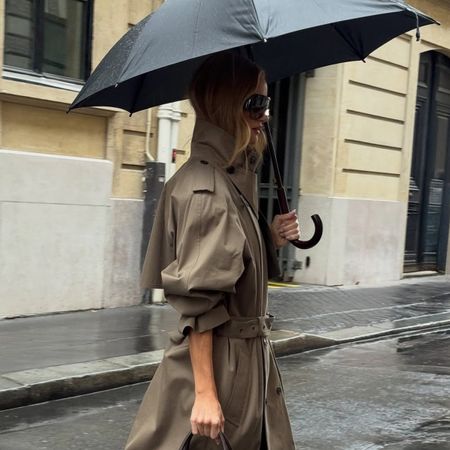 Rosie Huntington Whiteley walking in the rain wearing a trench coat and burgundy boots.