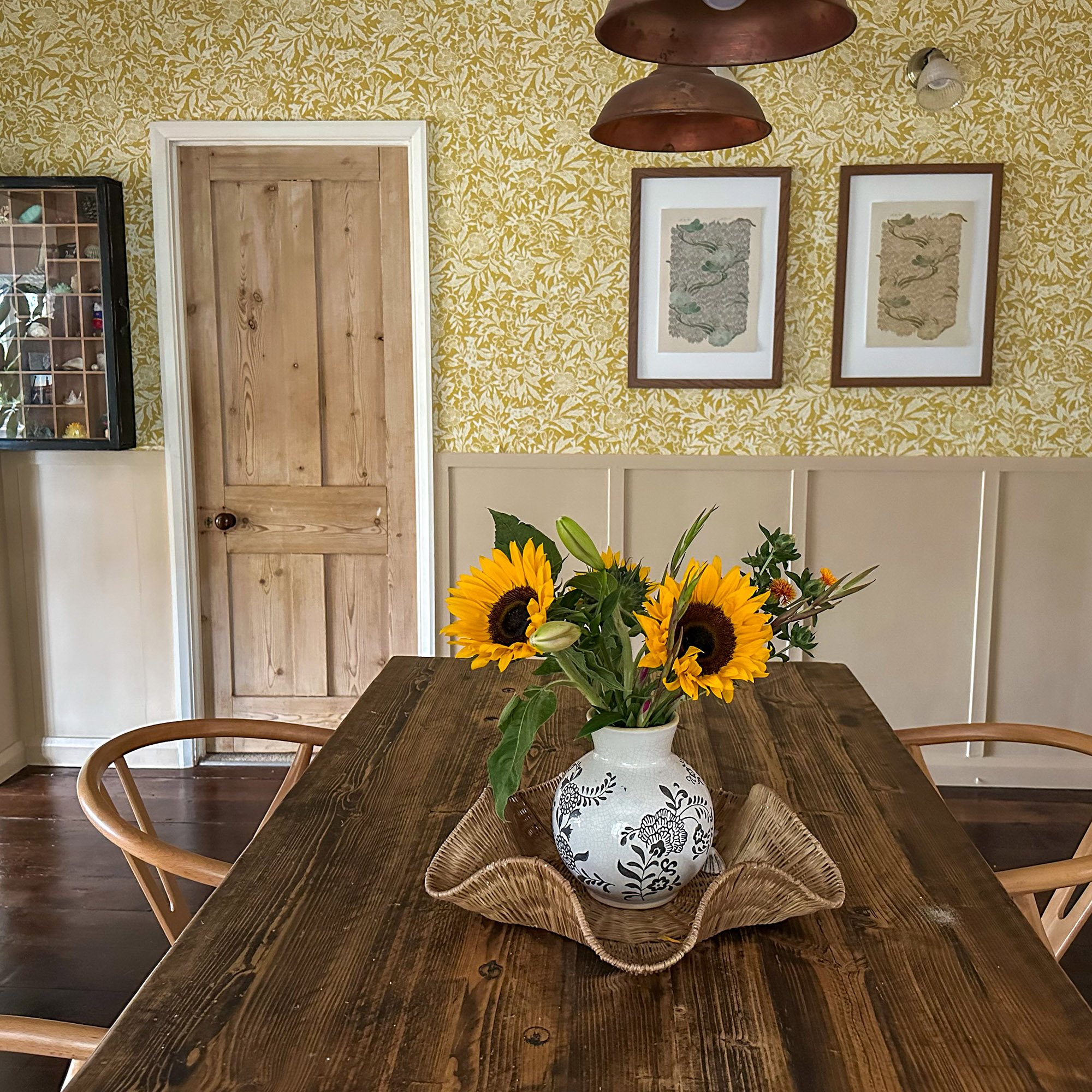 dining room with wood table and bowl of sunflowers in front of yellow patterned wall