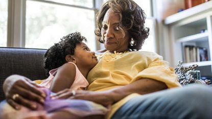 A grandmother cradles her granddaughter on the couch.