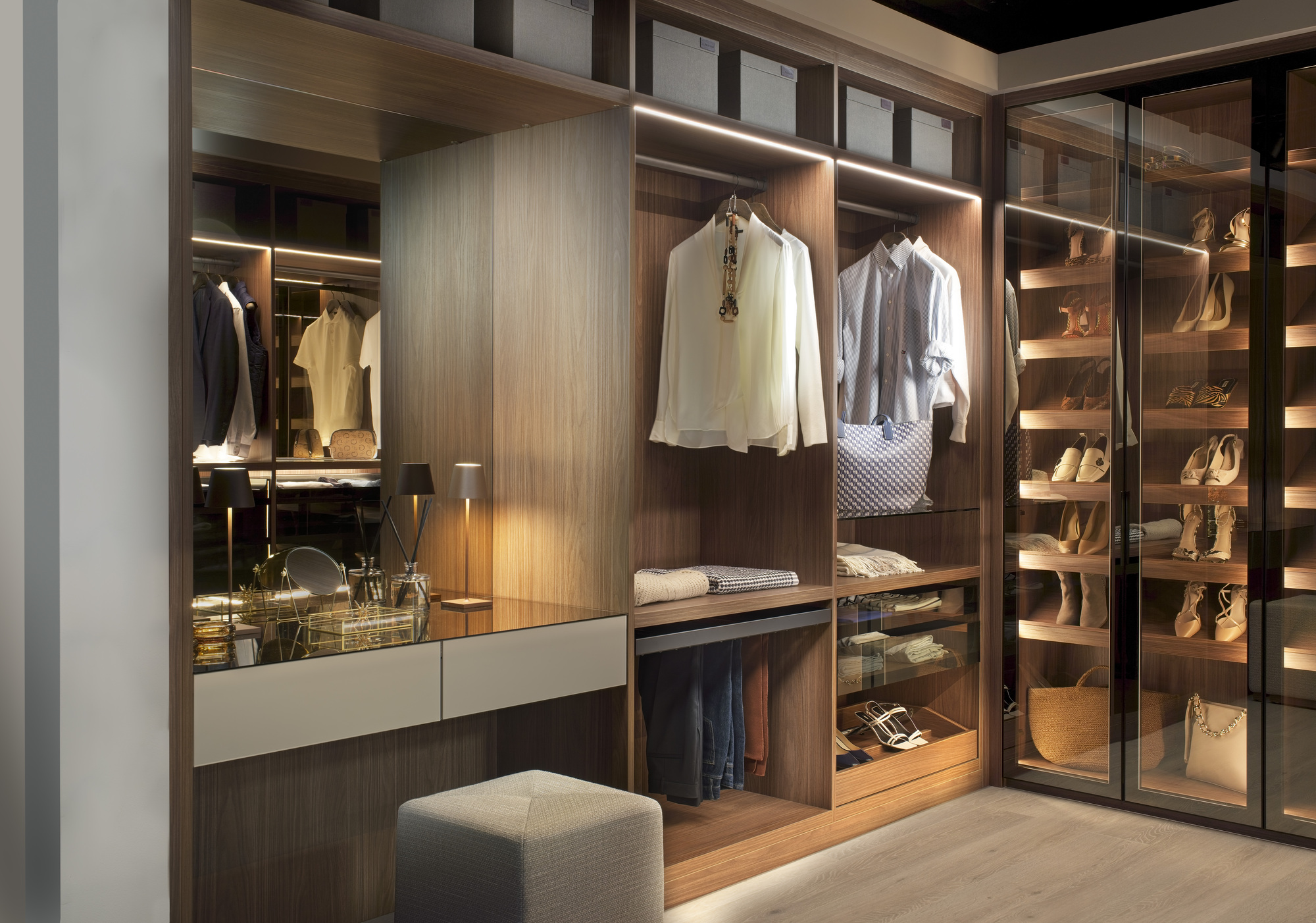 A large built-in closet of wood with rows of shoes on shelves, clothes hanging on rails, and a built-in dresser with a stool