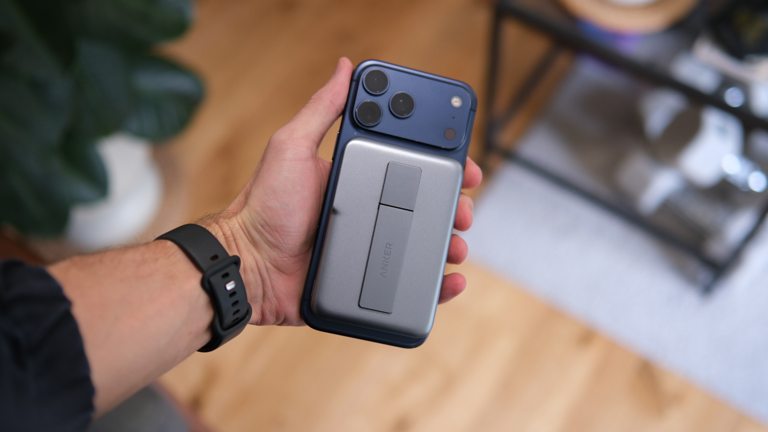 Anker MagGo Power Bank 2 Pro attached to the back of a blue smartphone and held in one hand, showing its built-in kickstand.