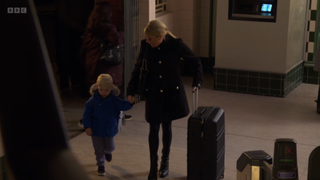 Sharon Watts holding Albie's hand at the tube station with a suitcase beside her.