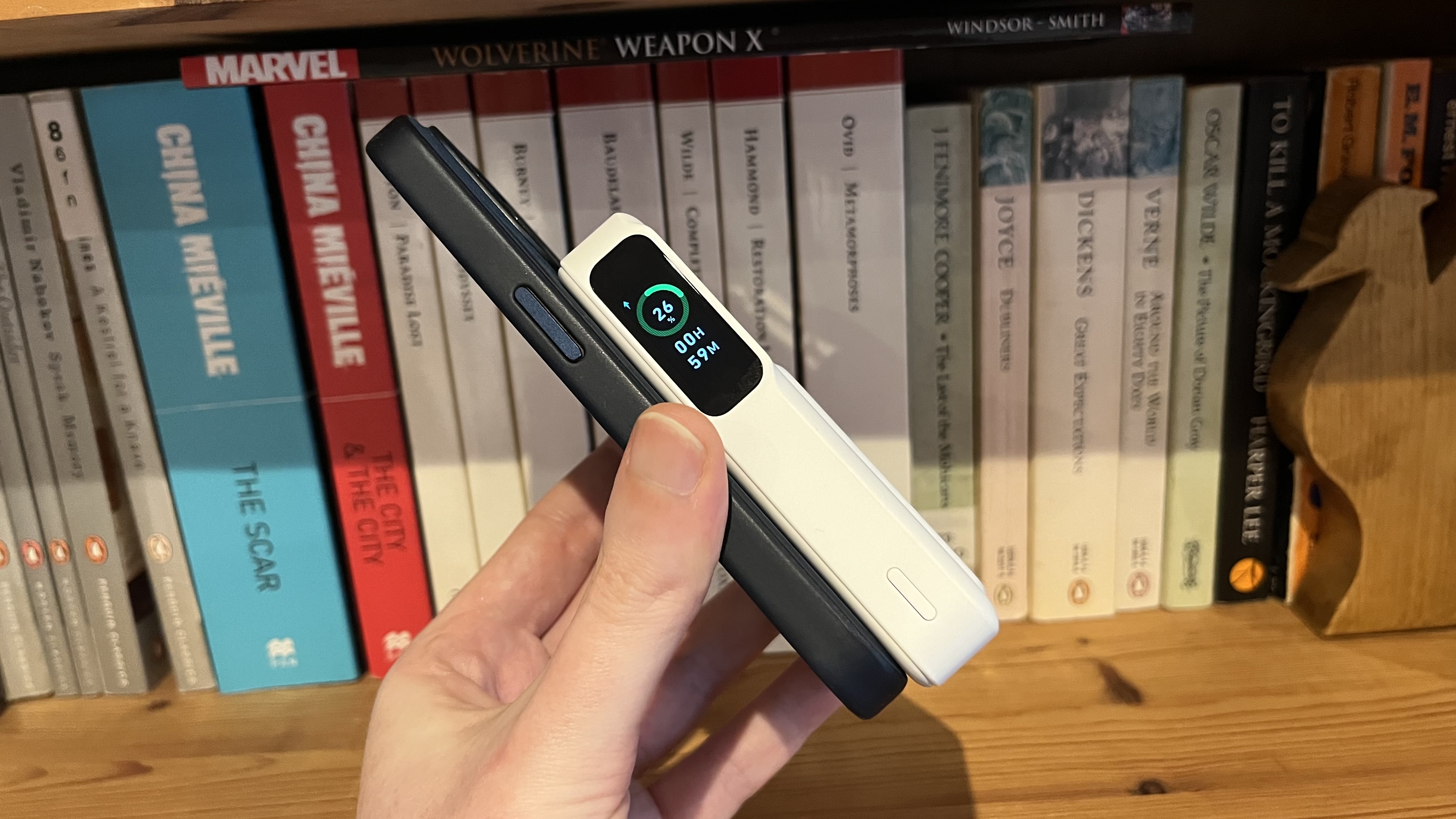 The Anker MagGo Power Bank (10K) connected to an iPhone 15 Pro on a wooden bookshelf