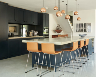 A shaker style kitchen with island, tan leather bar stools and nine copper ceiling pendant lights